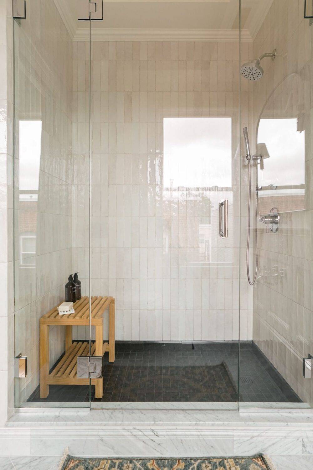 This contemporary shower features white handmade-look tile and a black mosaic tile floor.