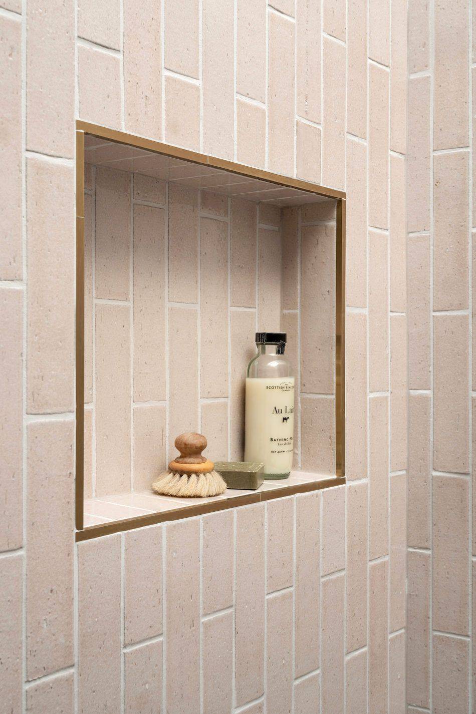 A shower niche featuring pink brick-look subway tile in a vertical offset layout and a rose-gold metal pencil liner.