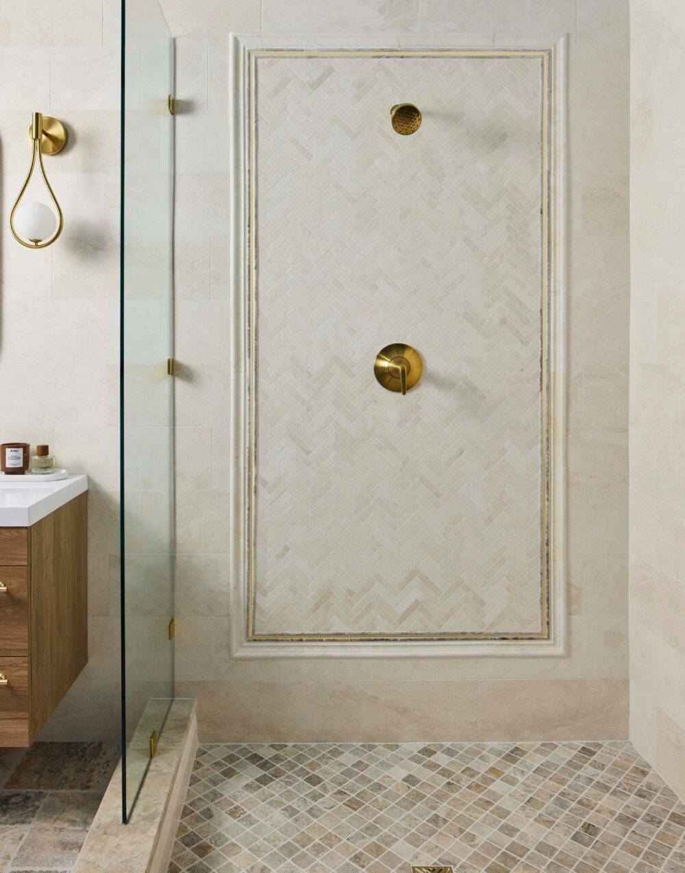 An elegant shower featuring a decorative picture frame with mosaic herringbone and marble and travertine tile.