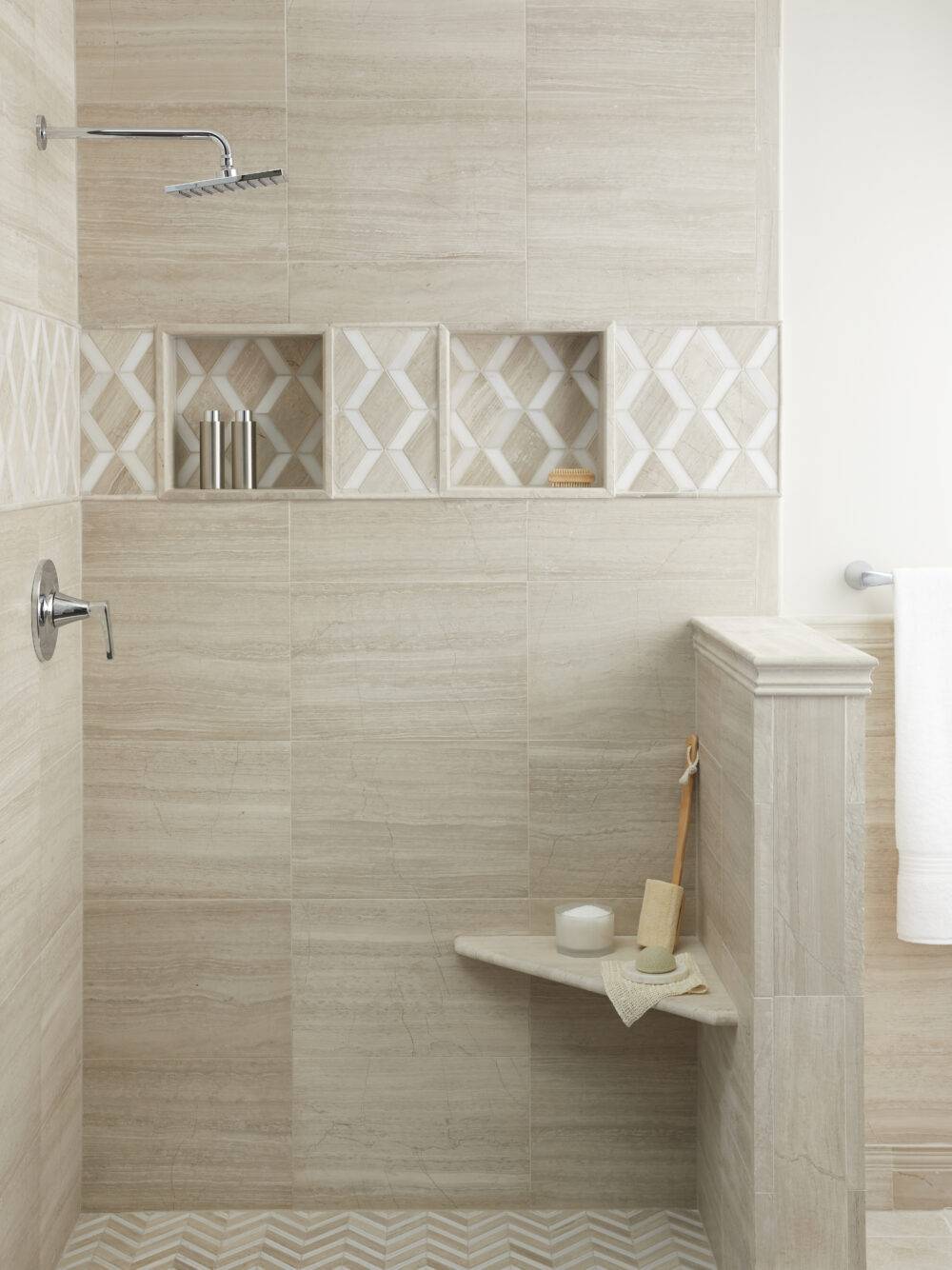Walk in shower in bathroom area tiled with a vein cut limestone of taupe and grey coloration in several sizes and mosaics alike. Mosaics are mixed with a white marble. Shower seat is same material. Fixtures are a polished chrome.