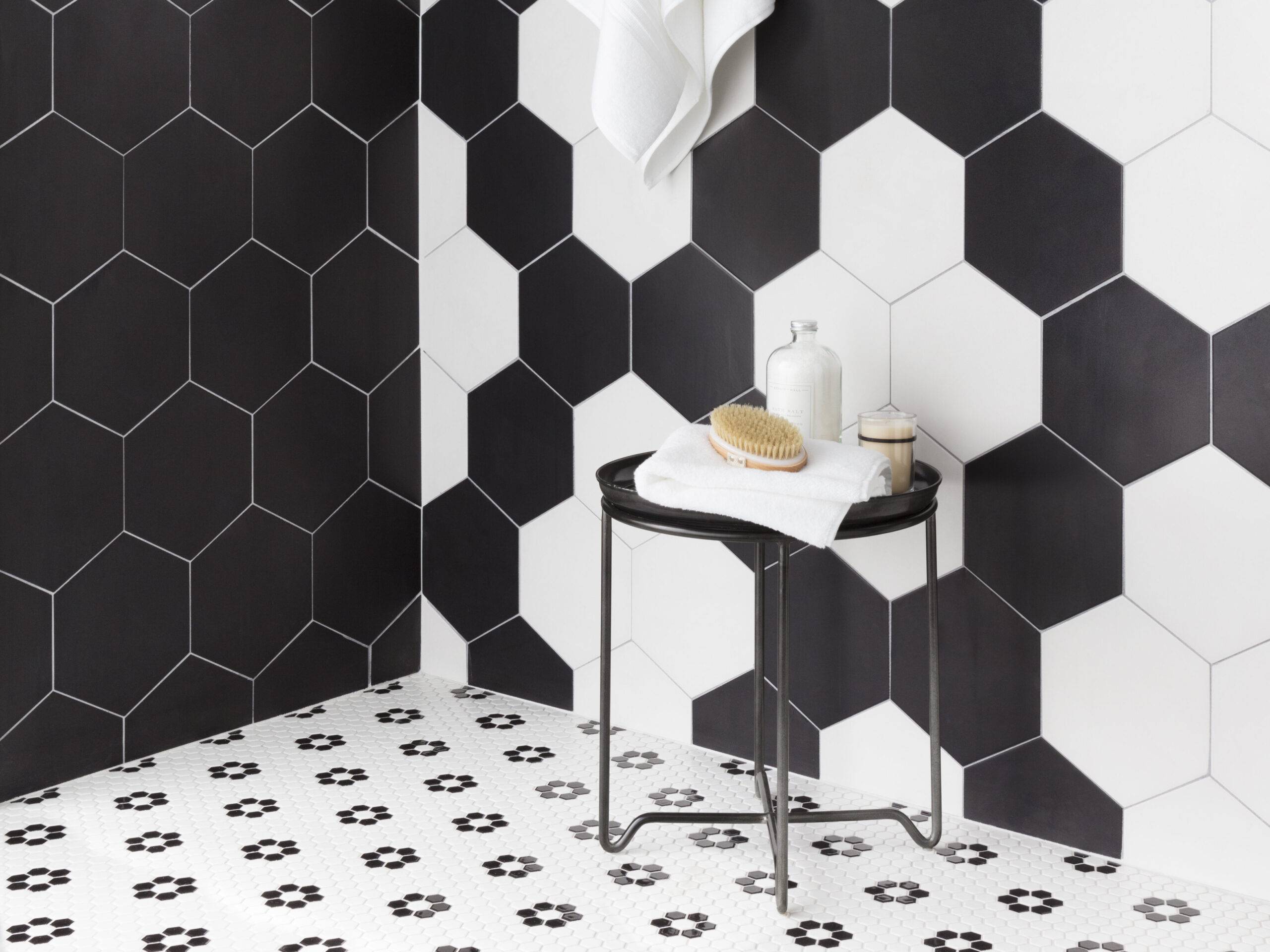 A shower with large black-and-white hexagon tile walls and small black-and-white hexagon floral patterned floor.